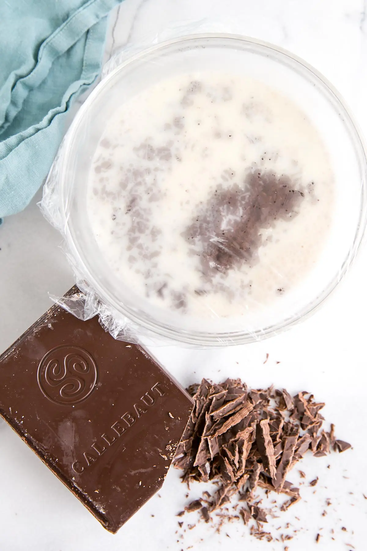 How to make Chocolate Ganache! A simple, two-ingredient recipe for a delicious frosting, filling, drip, or glaze. | livforcake.com Bowl of chopped chocolate and hot cream covered in plastic wrap.