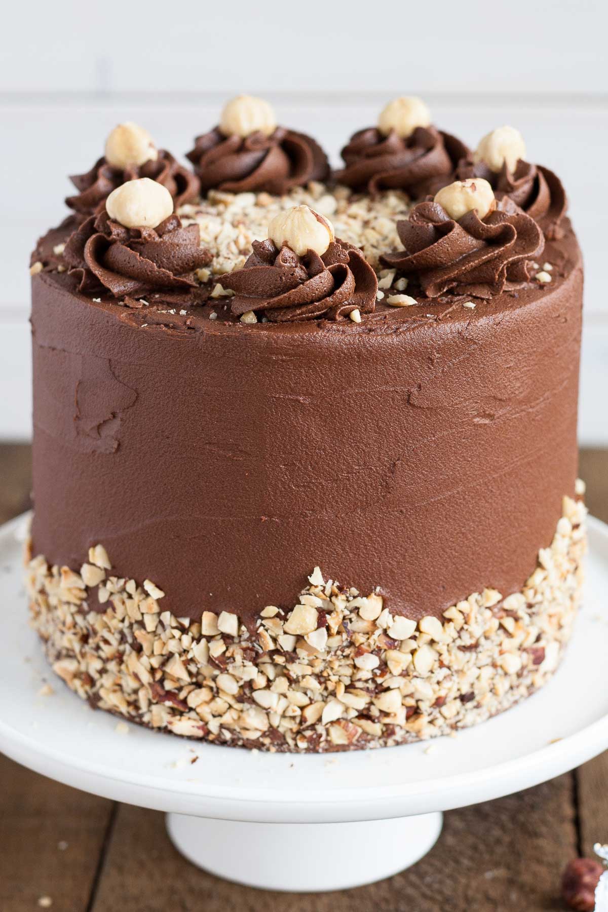 This Ferrero Rocher Cake is your favourite chocolate hazelnut treat in cake form! Chocolate hazelnut cake layers and with a Nutella buttercream. | livforcake.com Close up of the side of the cake showing the rosettes and hazelnuts.