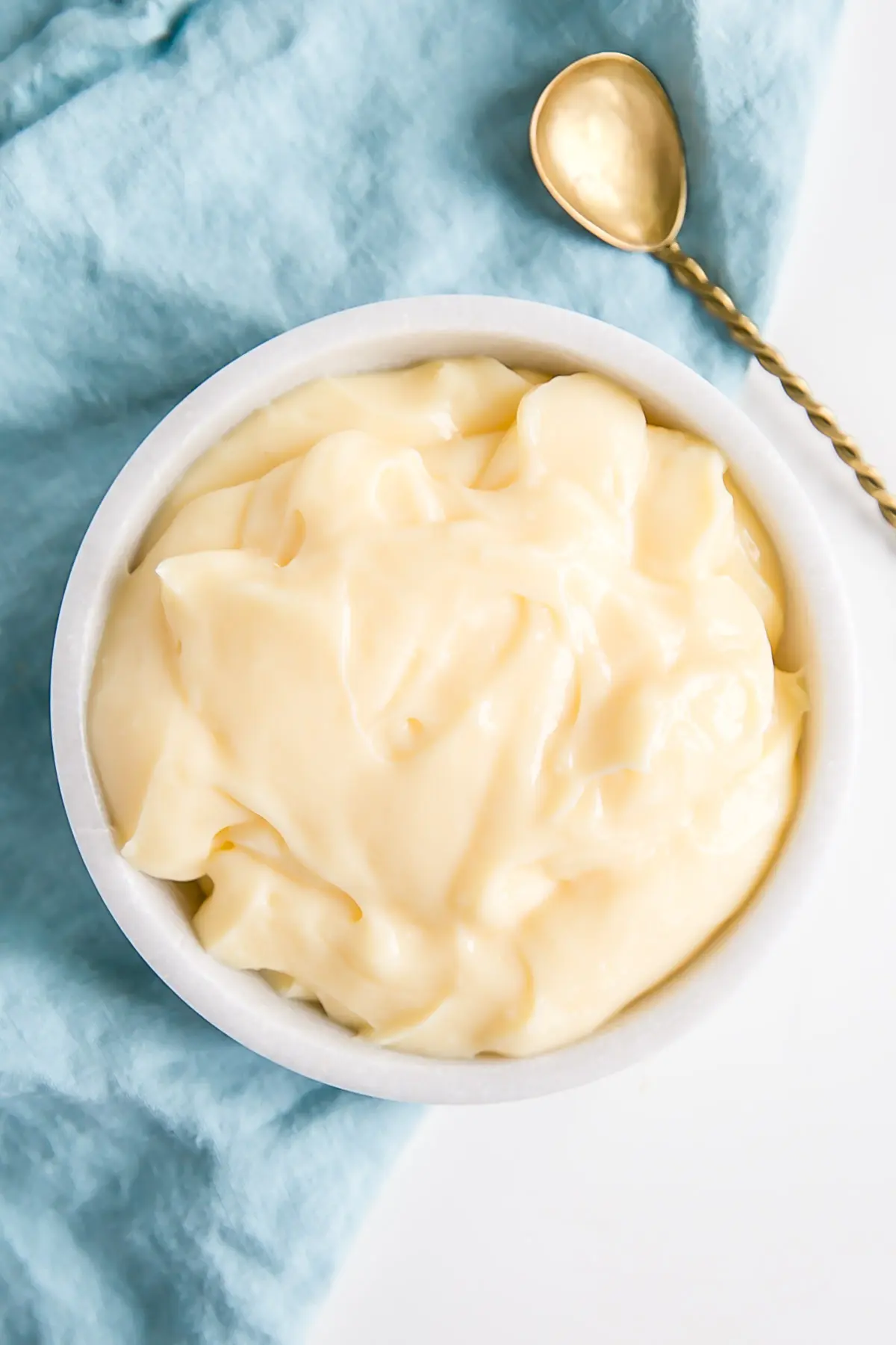 This easy Pastry Cream (Creme Patissiere) recipe is simple and delicious. A rich and creamy vanilla custard you can use in a variety of decadent desserts. | livforcake.com Pastry cream in a bowl with a gold spoon beside it.
