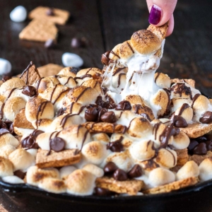 S'mores nachos in a cast iron skillet. Fingers pulling out one of the
